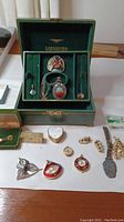 Wide view showing Longines jewelry box open with costume jewelry inside and additional pieces laid out in front on table.
