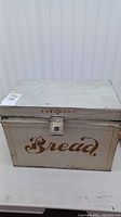 Front view of aged metal bread box with the word 'Bread' painted on the front.