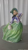 Front view of the Royal Doulton Autumn Breeze figurine showing the green flowing skirt, purple blouse, and blue bonnet with a smiling face