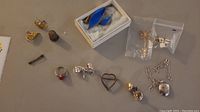 Full view of all jewelry pieces laid out on a table including rings, brooches, earrings, a chain with locket, a thimble, and a key.