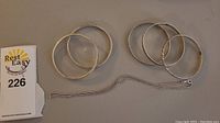 Five sterling silver bangles and one chain necklace arranged on a flat surface.