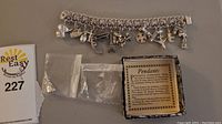 Full view of the sterling silver charm bracelet with all charms attached and additional charms in plastic bags next to identification tag