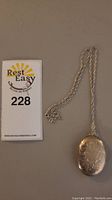 Full view of sterling silver locket pendant on twisted chain beside catalog number card