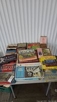 Overview of 15 vintage games and puzzles spread out on a table, showing multiple boxes with different titles and themes.
