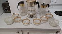 Full view of the coffee set on a kitchen counter showing 3 carafes, 6 glasses, and 5 bowls arranged in front