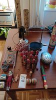 Photo showing assortment of vintage toys on table including French wooden skittles, wooden balls, metal toy phone, wooden man doll, and other wooden toys.