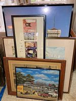 Stack of multiple framed and unframed art prints showing a variety of subjects and frame styles