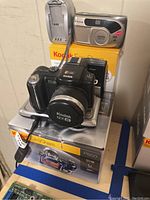 Photo showing Fujifilm Nezia camera, Kodak EasyShare P850 digital camera, charger, and dock stacked on original Kodak EasyShare P850 box.