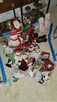 Overview of Christmas decorations including snowmen, moose, candle angels, and various ornaments piled on the floor
