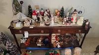 Wide view of two shelves with assorted Christmas decorations including figurines, mugs, candle holders, and two small lighted Christmas trees.