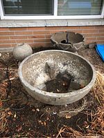 Front view showing large basin with tripod base, medium scalloped basin, and spherical cement piece placed on the ground outside a brick wall.