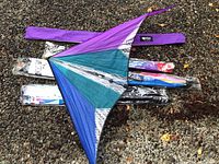 Prism Ignitor dual line sport kite with purple, teal and silver colors spread open with packaged stunt kites underneath on gravel surface.
