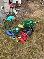 Lawn and garden equipment including Scotts Speedy Green 1000 seed spreader, Toro leaf blower model 51586, garden kneelers, watering pail and hose attachments on grass.