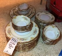 Stack of Noritake china including plates, bowls, and a gravy boat, showing floral pattern with gold trim.