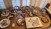 Wide view of 17 decorative plates featuring Norman Rockwell art and the related book on the table.