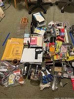 Wide view of the pile of office supplies including envelopes, pens, markers, tape dispensers, staplers, paper clips, scissors, and a magnifier.