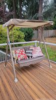 Full view of the two-seat porch swing with canopy on a wooden deck, with cushions arranged on the seat.