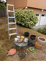 Photo showing the 6-foot aluminum step ladder, assorted gardening pots, small glass-top table, lawn animal figurines, metal edging, and small gardening tools arranged on grass.