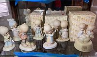 Seven Precious Moments porcelain figurines shown together on a shelf, three original boxes visible behind figurines. Figurines include children in various poses and outfits.