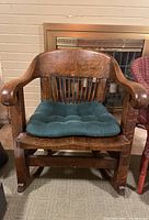 Front view of solid wood rocking chair showing curved armrests, vertical back spindles, split seat, and green tufted cushion tied to the seat.