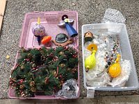 Overview of pink and clear plastic totes containing various decor pieces including Christmas wreath, glass ornaments, and metal/stone art pieces.