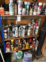 Full view of shelves displaying multiple spray paint cans, auto maintenance products, and chemical containers arranged on three wooden shelves.