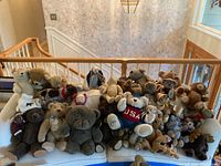 Photo showing 22 assorted stuffed bears arranged on a cushioned bench, showcasing variety in size, color, and clothing.