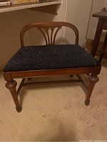 Front view of vintage wooden frame settee with dark cloth seat and arch backrest showing carved detail and turned legs with caster wheels