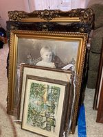 Stack of vintage ornate picture frames including a large one with a black and white photo of a child, plus several with art prints, visible evidence of vintage wear and tear.