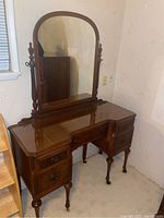 Full view of the vintage wooden vanity showing the arched mirror, drawer arrangement, and leg casters.