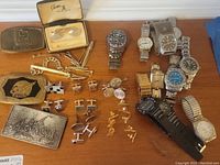 Overview of all items on table including watches, cufflinks, tie pins, and belt buckles arranged on wooden surface