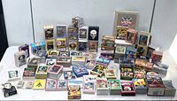 Wide view of approximately 60 sets of mostly non-sports trading cards in various colorful boxes and cases arranged on visible surface.