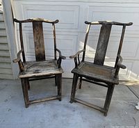 Front view of two weathered Chinese elm wood arm chairs showing shape, design, and wear on seats and backs.