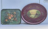 Front view showing the two metal trays; oval with landscape painting and rectangular with flower bouquet painting