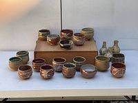 Full view of the 21 pieces including tea bowls and small vessels arranged in front of a wooden box, showing varied glaze colors and shapes.