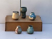 Full view of the five pots arranged on a cardboard base showing variety of shapes and glazes