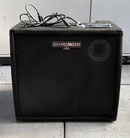 Front view of black Behringer amplifier with metal grille and Behringer logo.