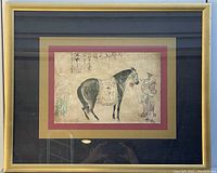 Photo of the framed Chinese print showing a detailed image of a horse with a rider and calligraphy stamps on beige paper, mounted on gold/red matting within a gold frame.