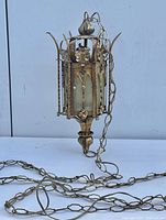 Photo showing the full hanging lantern with chain, gold iron frame, and translucent glass panes against a neutral background.
