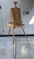 Full view of the wooden easel set up with tripod legs, showing the storage drawer and panel holder.