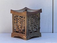 Front view of the weathered iron Japanese garden lantern showing decorative leaf cut-out panels and curved roof with ring handle.
