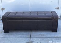 Front view of the brown leather settee bench showing tufted cushion top and block feet on a concrete floor.
