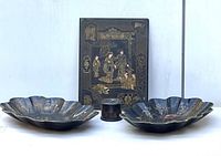 Front view of all four items showing two scalloped trays, one rectangular panel, and one round trinket box, all black with gold and colored painted details.