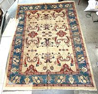 Full view of large oriental carpet with cream, red, brown and blue floral motifs and borders.
