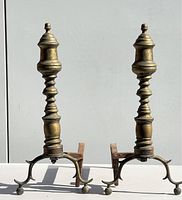 Front view of both brass and wrought iron andirons showing turned brass columns and three-legged curved wrought iron base with ball feet.