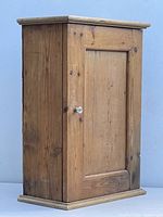 View of the pine wood wall cabinet cupboard showing front with door closed and white knob.