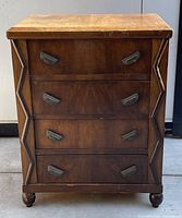Front view of small wooden 4 drawer chest showing geometric carved detailing on vertical edges and metal handles on drawers, with surface scratches visible on top.