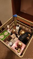 Milk crate containing various Avon collectible bottles, some in original boxes, assorted pins, and small decorative music boxes.