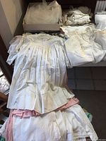 Overview of vintage white baby gowns and wedding veil folded on a table showing pleats and lace details with some discoloration.