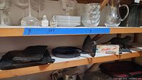 Shelf containing the cornbread stick pan, square ridged griddle, sad iron, Rocket nutcracker with box, and dog-shaped nutcracker.